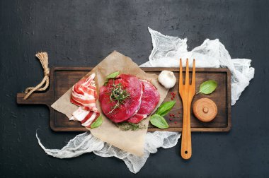 Parşömen kağıt üzerine kahverengi kesme tahtası üzerinde çiğ et (biftek). Siyah arka plan, metin için yer.