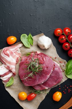 Parşömen kağıt üzerine çiğ et (biftek). Çok renkli domates ve fesleğen yaprakları yanında. Makro çekim. Metin için yer