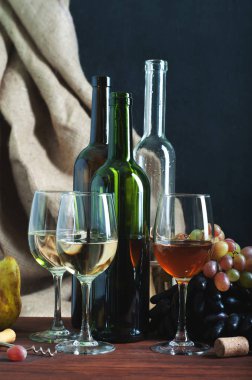 Şişe ve bardak kahverengi ahşap tahta üzerinde şarap. Koyu mavi zemin üzerine tutuyordu. Armut ve üzüm yanında. Yazarın rötuş