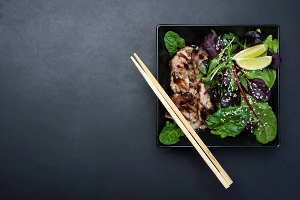 Delicious hearty lunch. Baked ham (pork) with teriyaki sauce and mixed herb salad (spinach, arugula, beet leaves), oil, soy sauce, lemon juice and sesame seeds