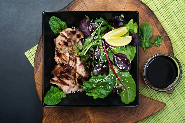 Delicious hearty lunch. Baked ham (pork) with teriyaki sauce and mixed herb salad (spinach, arugula, beet leaves), oil, soy sauce, lemon juice and sesame seeds