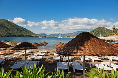 Marmaris, Türkiye'de plaj. Hasır ve beyaz şezlong, parlak mavi gökyüzü ve deniz şemsiyeleri. Seyahat ve tatil konsepti