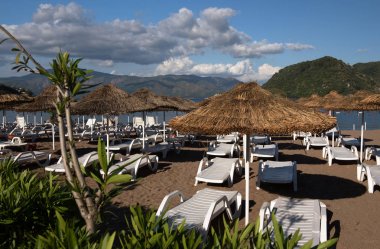 Marmaris, Türkiye'de plaj. Saman ve beyaz şezlong, parlak mavi gökyüzü ve deniz şemsiyeleri. Seyahat ve tatil konsepti