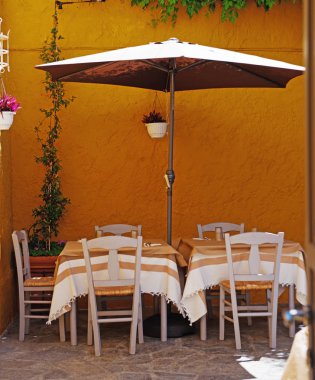 Sokak Kafe.' Masalar, sandalyeler ve parlak turuncu duvara karşı bir şemsiye. Yunanistan, Rodos