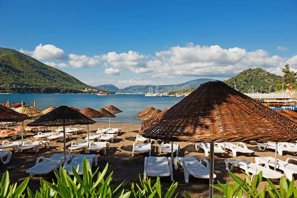 Marmaris, Türkiye'de plaj. Hasır ve beyaz şezlong, parlak mavi gökyüzü ve deniz şemsiyeleri. Seyahat ve tatil konsepti