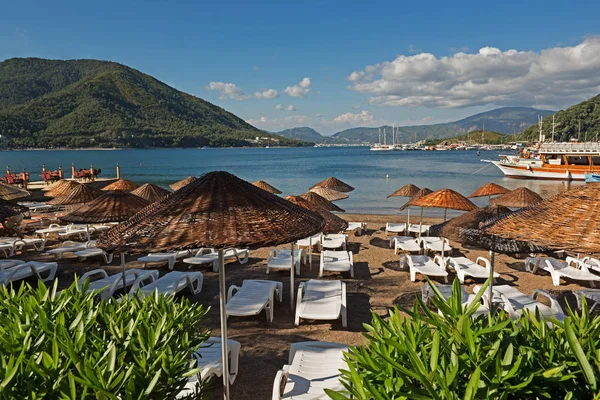 Marmaris, Türkiye'de plaj. Hasır ve beyaz şezlong, parlak mavi gökyüzü ve deniz şemsiyeleri. Seyahat ve tatil konsepti