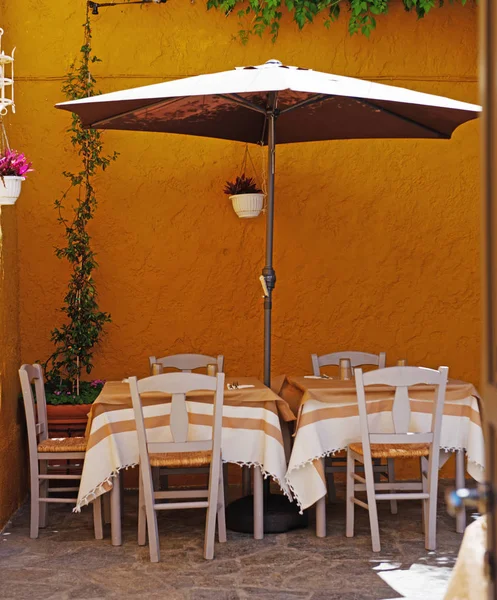 Sokak Kafe.' Masalar, sandalyeler ve parlak turuncu duvara karşı bir şemsiye. Yunanistan, Rodos
