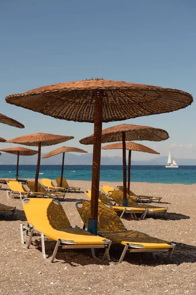 Rodos adasındaki plaj. Hasır ve sarı yatak, parlak mavi gökyüzü ve deniz şemsiyeleri. Seyahat ve tatil konsepti — Stok fotoğraf