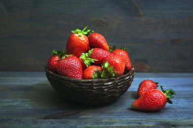Gri-mavi ağaçlık üzerinde kil bir kapta sulu taze kırmızı çilek
