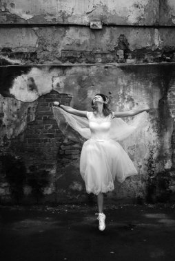 Gelinlik içinde güzel bir gelin ve duvak yıkılmış bir duvarın arkasında süzülüyor. Siyah beyaz fotoğraf, seçici keskinlik