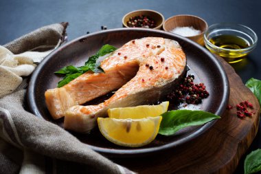 Kahverengi bir tabakta koyu arkaplanda pişmiş somon bifteği. Yan görünüm