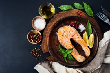 Kahverengi bir tabakta fırında somon bifteği, fesleğen yaprağı ve baharatların yanında. Karanlık arka plan. Metin için yer