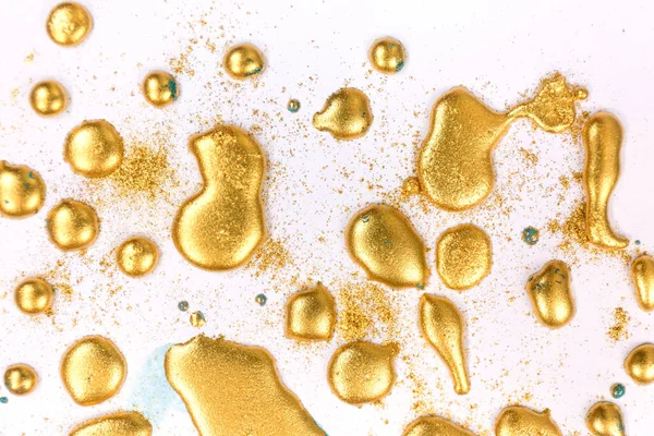 Golden ink drops on white paper background.