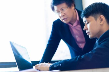 İş ortağı ofisinde bilgisayarında çalışan genç Asyalı işadamı büyük parlak pencere, seçici odak yakınındaki ve tonlama, takım çalışması iş tema veya kavram için iyi renk bulanıklık