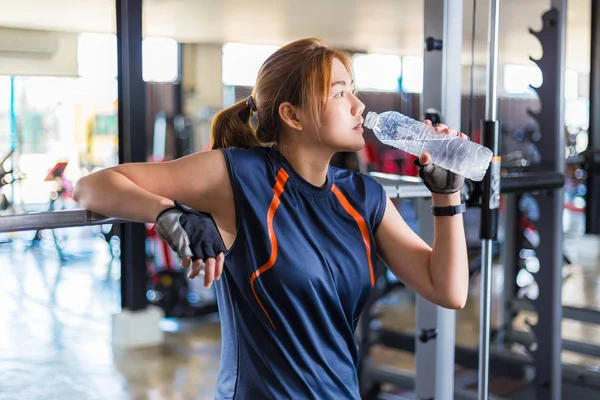 Young Asian woman working out and doing fitness training at a local gym taking a rest to drink water, good for young healthy lifestyle or fitness concept