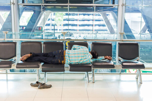 БАНГКОК, Таиланд - 21 июля 2018 года - уставший мужчина спит на местах в аэропорту Суварнафоми в Бангкоке, Таиланд, 21 июля 2018 года
