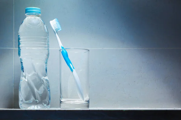 清洁的白色牙刷与蓝色修剪在明确的饮水玻璃和一瓶饮用水在货架上 点燃与最高光 良好的健康牙齿和牙齿或清洁生活方式的概念 — 图库照片