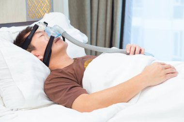 CPAP maske takıyor, hava hortumu için bağlanma, onun yatak odası ve geniş pencere, iyi uyku apnesi hikayesi için yatağında uyuyan Asyalı adam
