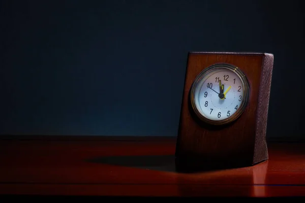 Old business desk clock on wooden table at night with the time showing almost midnight, blue tone background to show night time with copy space, good for time related concept