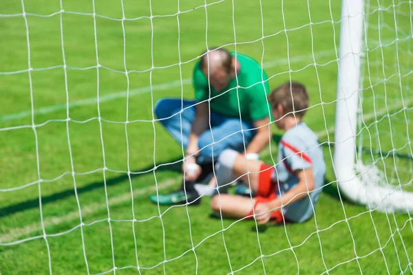 Blurred picture of a young injured male soccer or football player being treated by male team physician in front of the team goal at an outdoor game