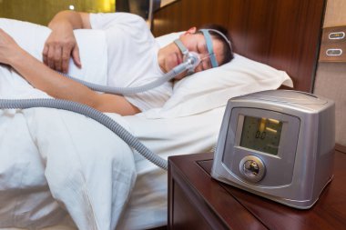 Cpap makine başucundaki sonraki yatağa uyku Asya ile oturan adam giyen şapka Tüp, iyi uyku apnesi tema için hava bağlı