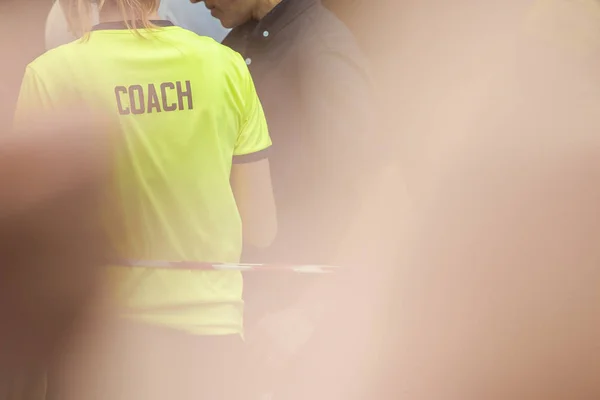 Back view of female sport coach with word COACH written on her shirt's back