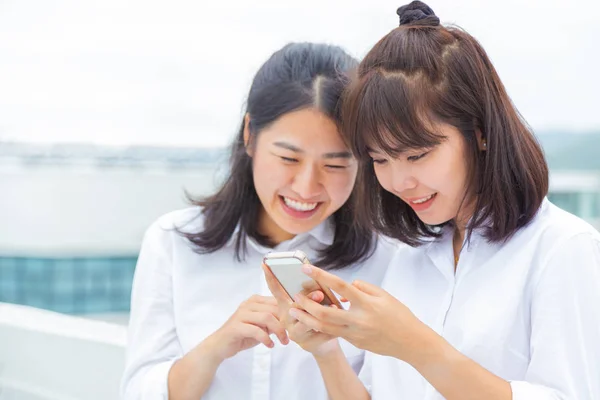 Two young woman enjoy using their smart phone to connect to digital social media, good for young lifestyle or modern technology concept, selective focus on hands holding the phone