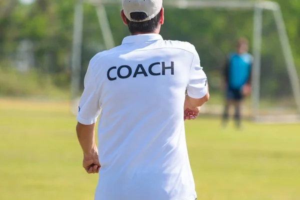 Back of football coach wearing white COACH shirt at an outdoor sport field coaching his goalie player during a game, good for sport or coaching concept