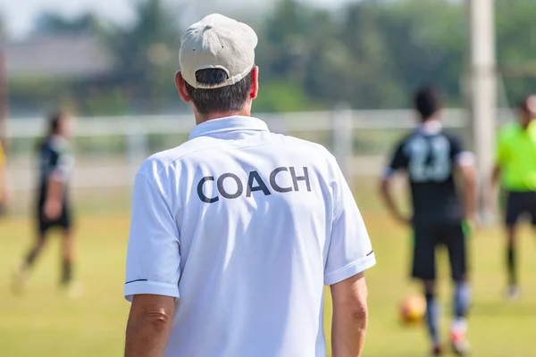Back of male football coach wearing white COACH shirt at an outdoor sport field coaching his team during a game, good for sport or coaching concept