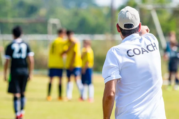 Back of male football coach wearing white COACH shirt at an outdoor sport field coaching his team during a game, good for sport or coaching concept