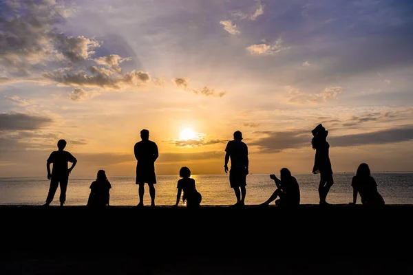 Silueta de personas relajadas viendo amanecer colorido en una playa — Foto de Stock