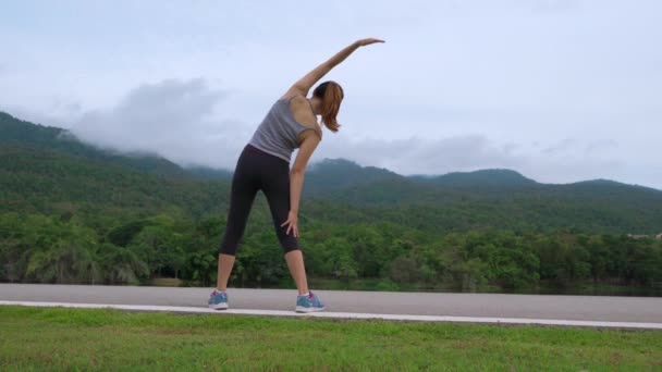 Krásná Asijská sportovec dělá ranní cvičení u jezera s výhledem na jezero a hory na pozadí, zdravý životní styl