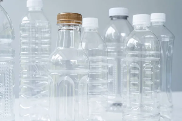Пластикові пляшки різних форм і розмірів на білому столі і фоні — стокове фото