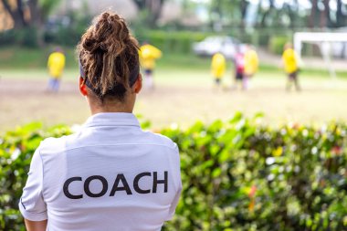 Kadın futbol, futbol, beyaz koç tişörtlü koç takımının açık hava futbol sahasında oynamasını izliyor.