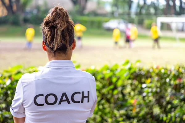 Vue arrière d'une footballeuse, d'un entraîneur en chemise blanche qui regarde son équipe jouer sur un terrain de football extérieur — Photo