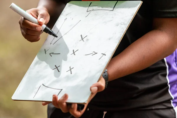 Primer plano del plan de juego de escritura a mano del entrenador deportivo femenino en una pequeña pizarra blanca en el campo antes del juego — Foto de Stock