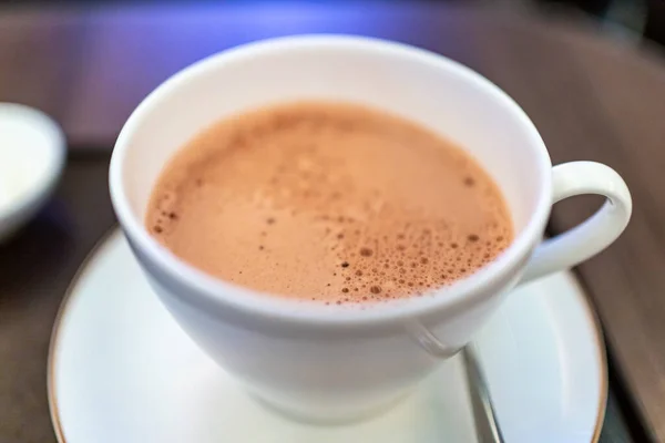 A cup of hot chocolate in white cup with lots of foamy bubbles