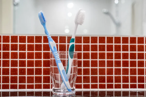Two blue and green clean toothbrushes in clear glass on bathroom counter top, dental concept, selective focus
