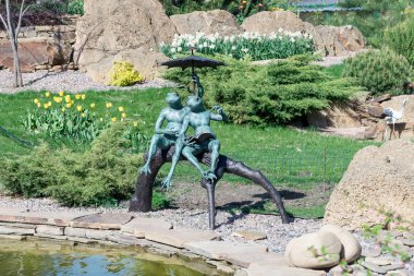 Parktaki gölün yanındaki şemsiyenin altında birbirine aşık iki kurbağa heykeli..