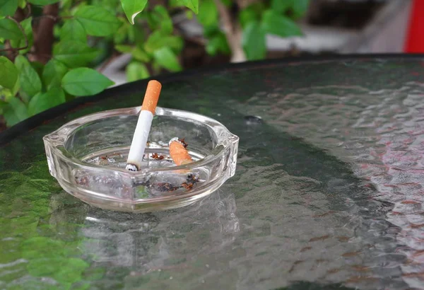 放在桌子玻璃上的烟灰缸里的香烟 — 图库照片