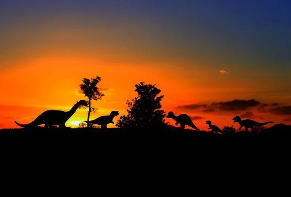 Siluetas de dinosaurios en el bosque sobre el fondo del atardecer — Foto de Stock