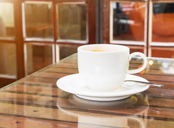 Kávéscsésze fehér az üvegasztalon fából és cement fal háttér — Stock Fotó