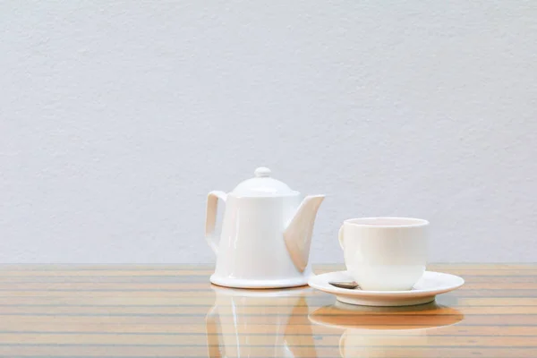 Kaffeetasse und Teekanne weiß auf dem Glastisch Holz- und Zementwand Hintergrund — Stockfoto