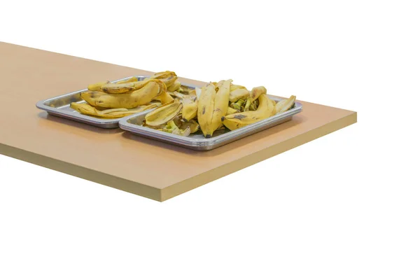 Banánhéj fa asztalon, elszigetelt fehér háttérrel a tálcában — Stock Fotó