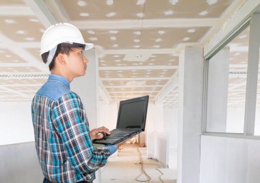 Dizüstü bilgisayar kullanan ve iç yapı denetimine beyaz kaskla giren bir mühendis.