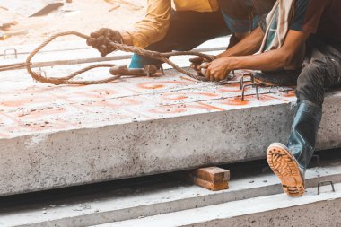 İşçiler inşaat sahasında asılarak beton sütunları taşıyorlar.