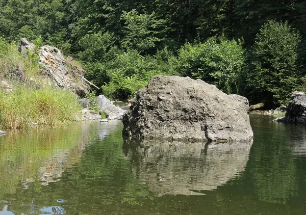 big rock in the river reflecting on the water surface, Moravka river, Czech Republic