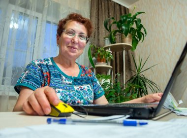 Yaşlı gülümseyen bir kadın oturan ve onun laptop çalışan