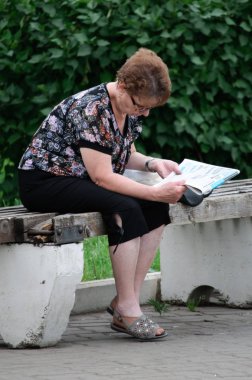 Vyazma, Rusya - 02 Temmuz 2011: Parktaki bankta otururken gazete okuyan yaşlı kadın