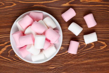 Koyu ahşap masadaki bir tabağın üzerinde beyaz ve pembe şekerleme. Üst görünüm